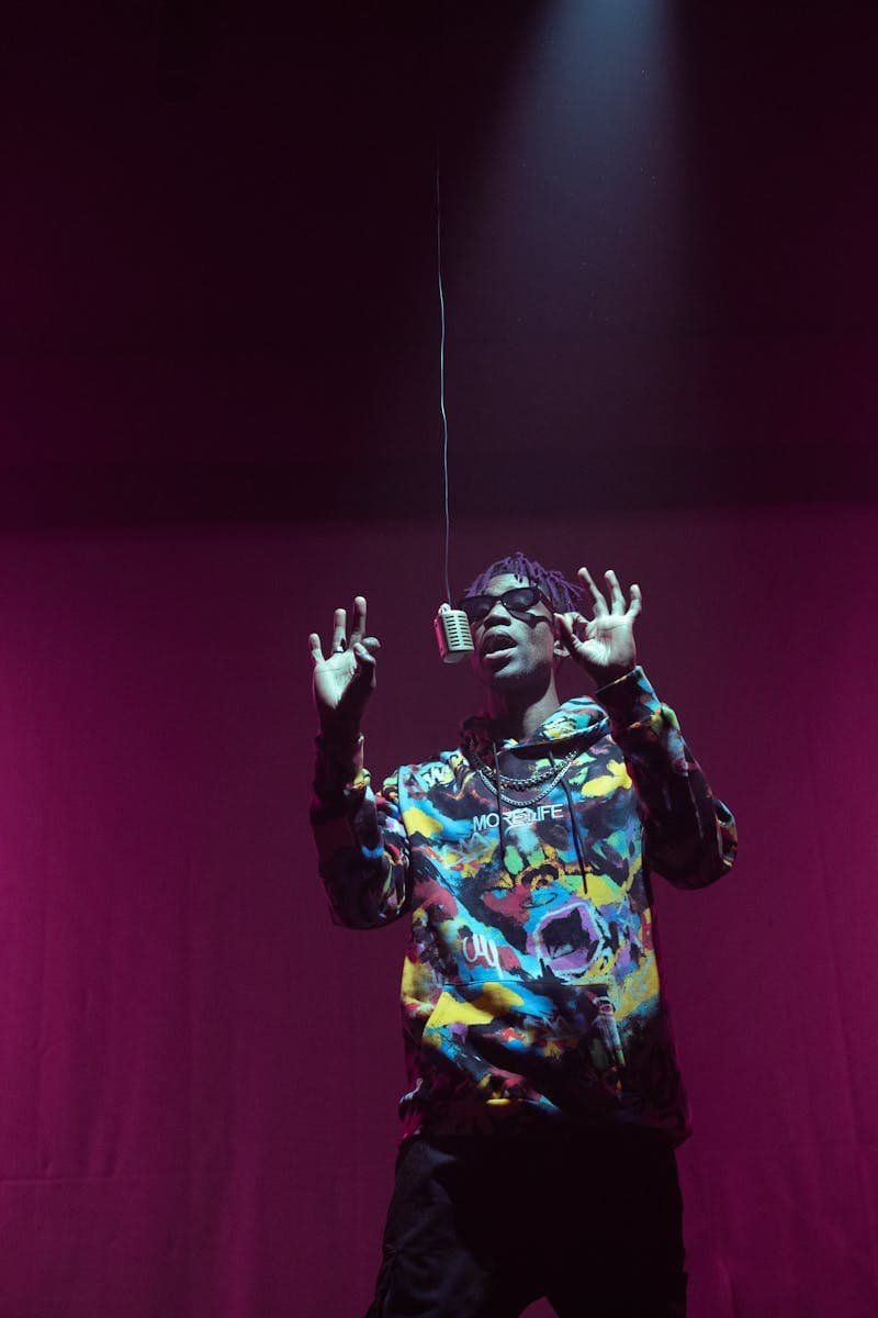 Energetic performance of a hip hop artist under dramatic stage lighting with vibrant hoodie.