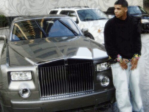 Stevie The Manager standing next to a luxury black car in an urban setting.