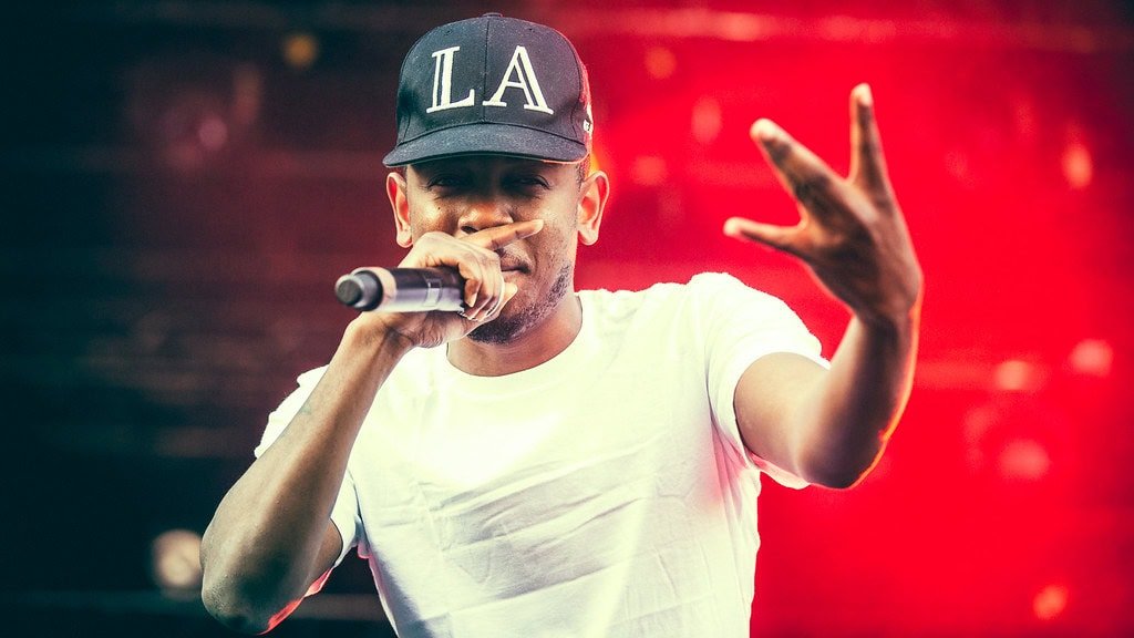 Stevie The Manager rapping on stage with a microphone, wearing a LA cap.