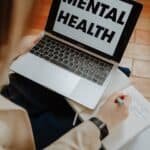 A woman engaging in an online mental health session on a laptop.