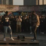 Street dance battle with Stevie The Manager and another dancer on a graffiti-covered wall.