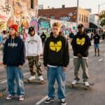 Group of young skateboarders in streetwear at graffiti-covered urban area.